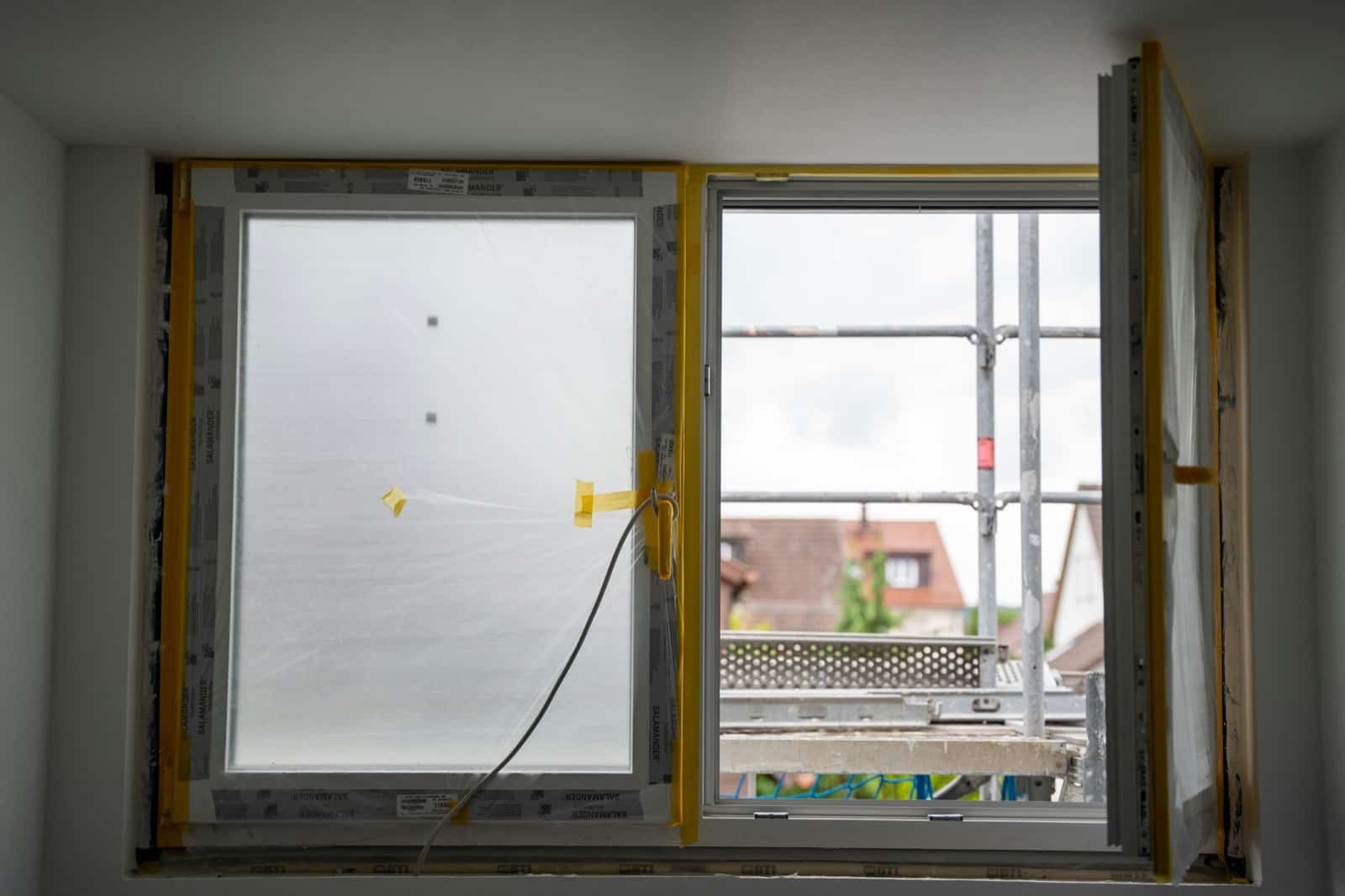Fenêtre neuve en cours de pose avec son film plastique de protection, vue depuis un échafaudage de chantier