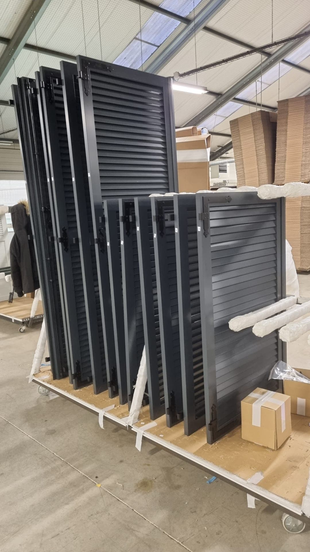 Persiennes aluminium anthracite à lames fixes, rangées sur un chariot d’atelier