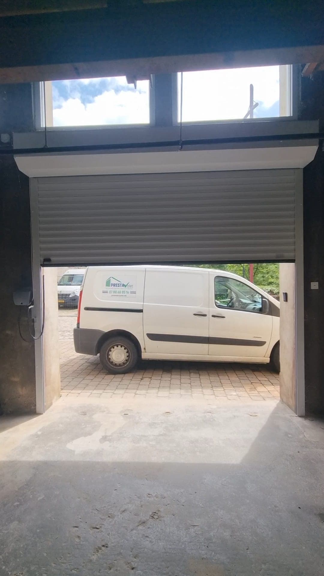 Porte de garage enroulable posée sous linteau, ouverte sur le fourgon de l’entreprise