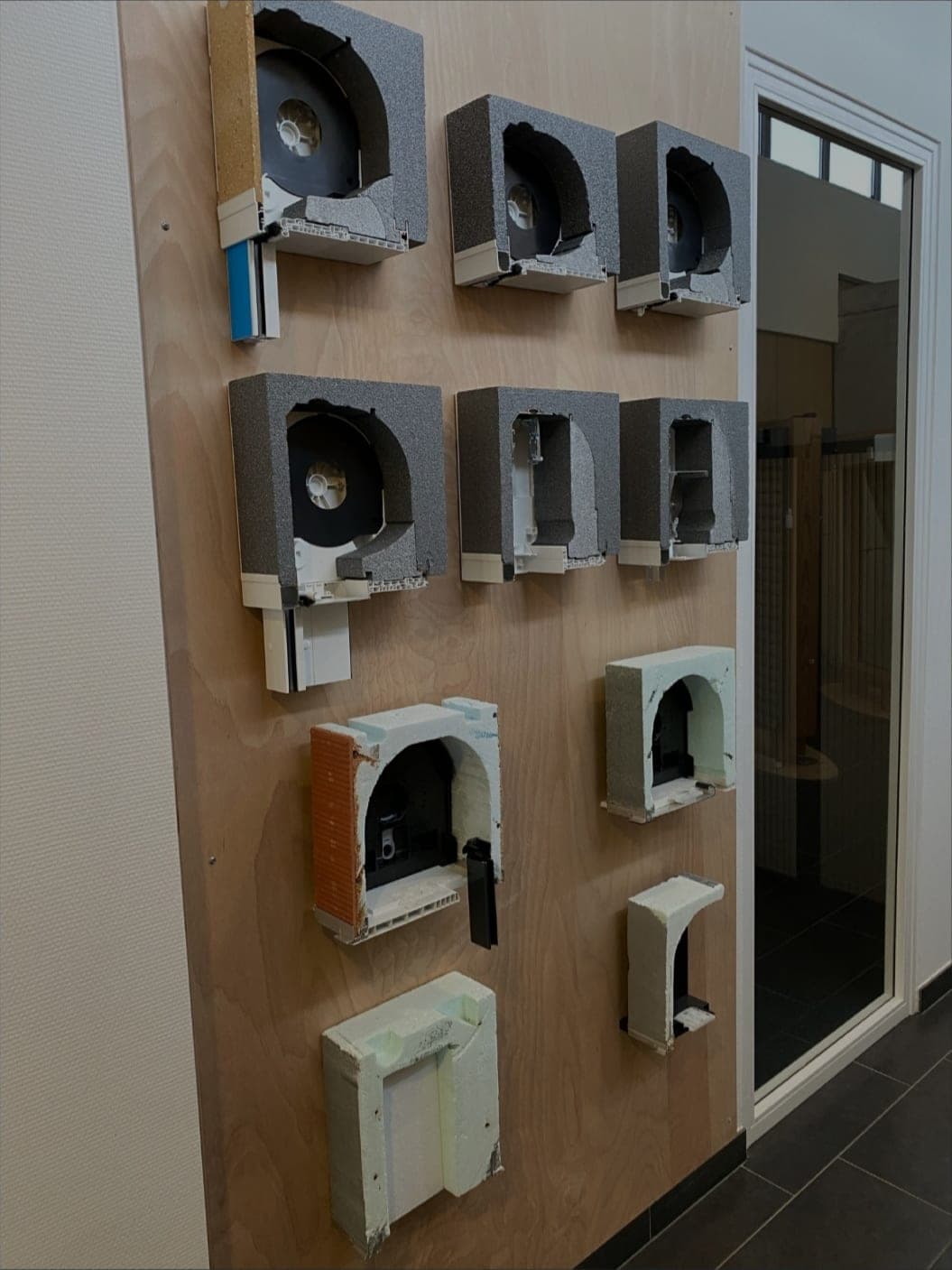 Mur d’exposition présentant une douzaine de coffres de volets roulants en coupe