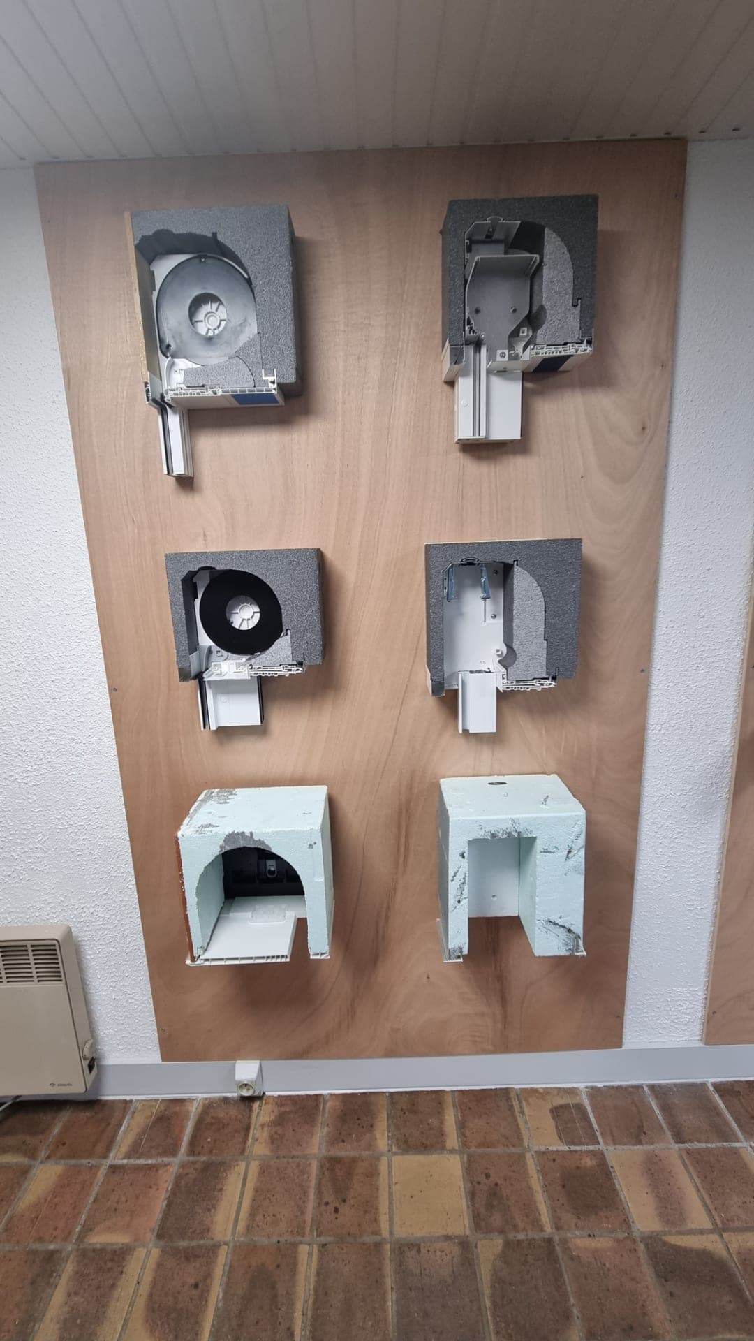 Coffres de volets roulants ouverts sur leurs mécanismes, exposés au mur du showroom