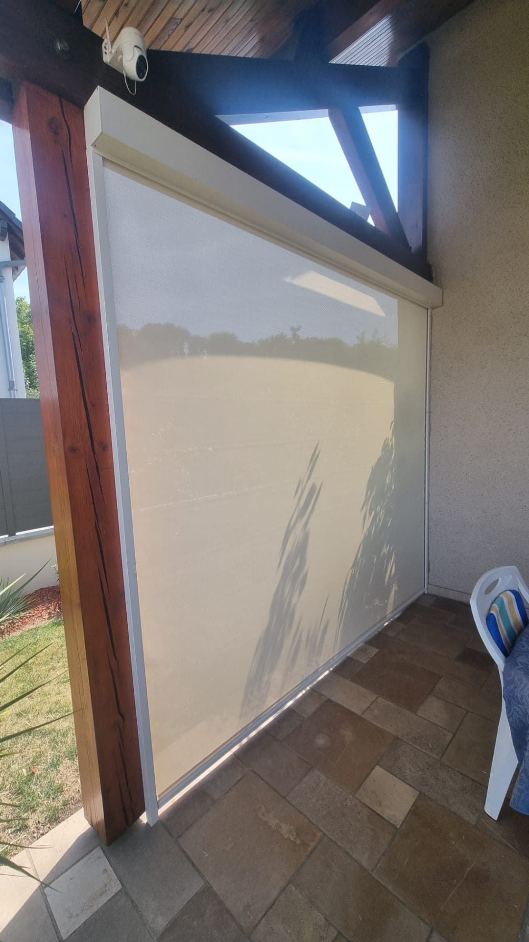 Store screen beige tendu sous une pergola en bois, filtrant la lumière du jardin