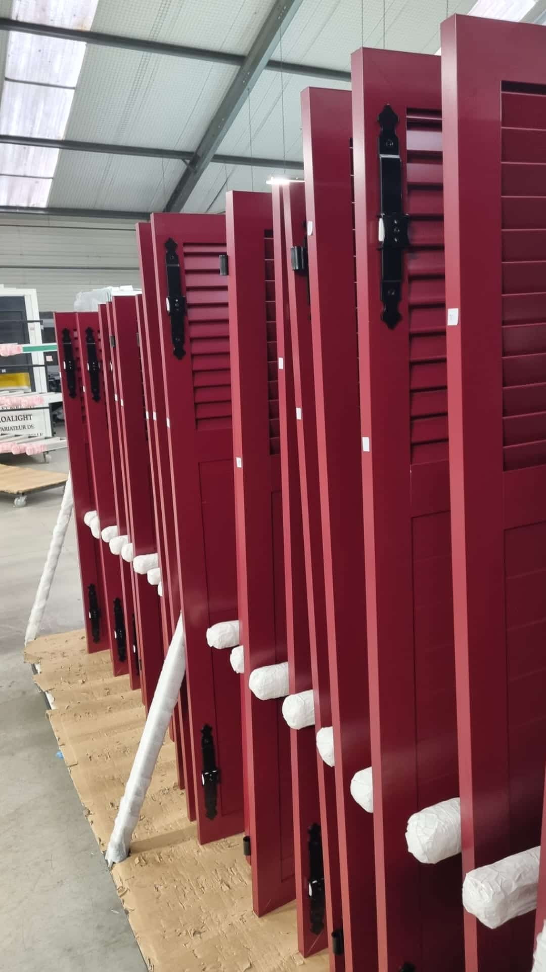 Volets battants aluminium rouge bordeaux alignés à l’atelier avant leur pose