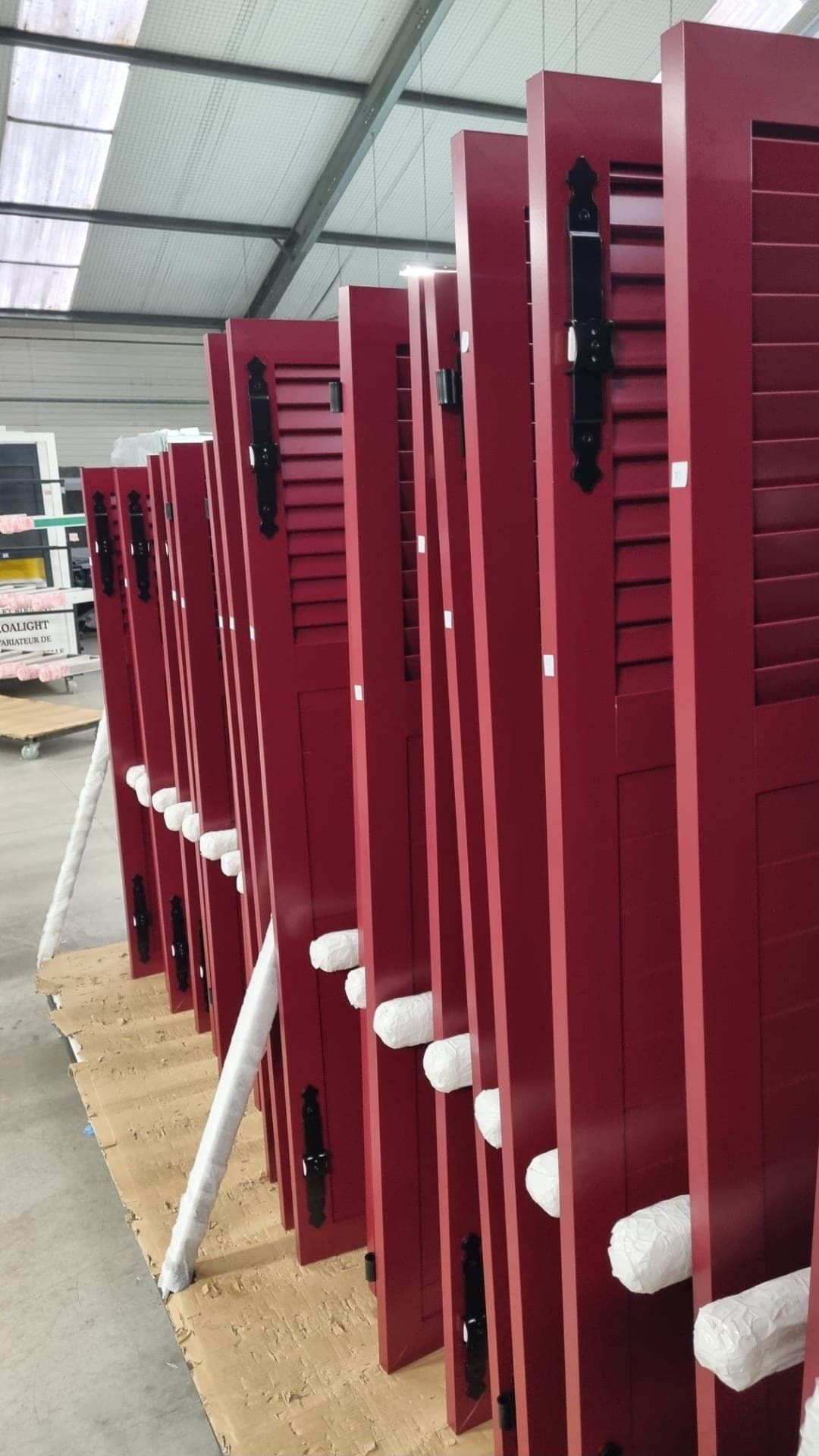 Série de volets battants aluminium rouge bordeaux alignés à l’atelier avant livraison