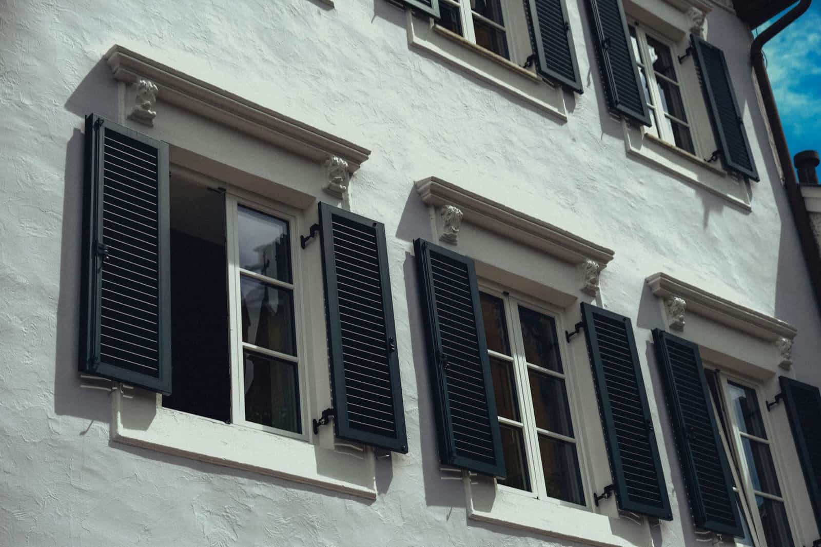 Façade blanche avec volets battants ouverts et fermés sur ses fenêtres